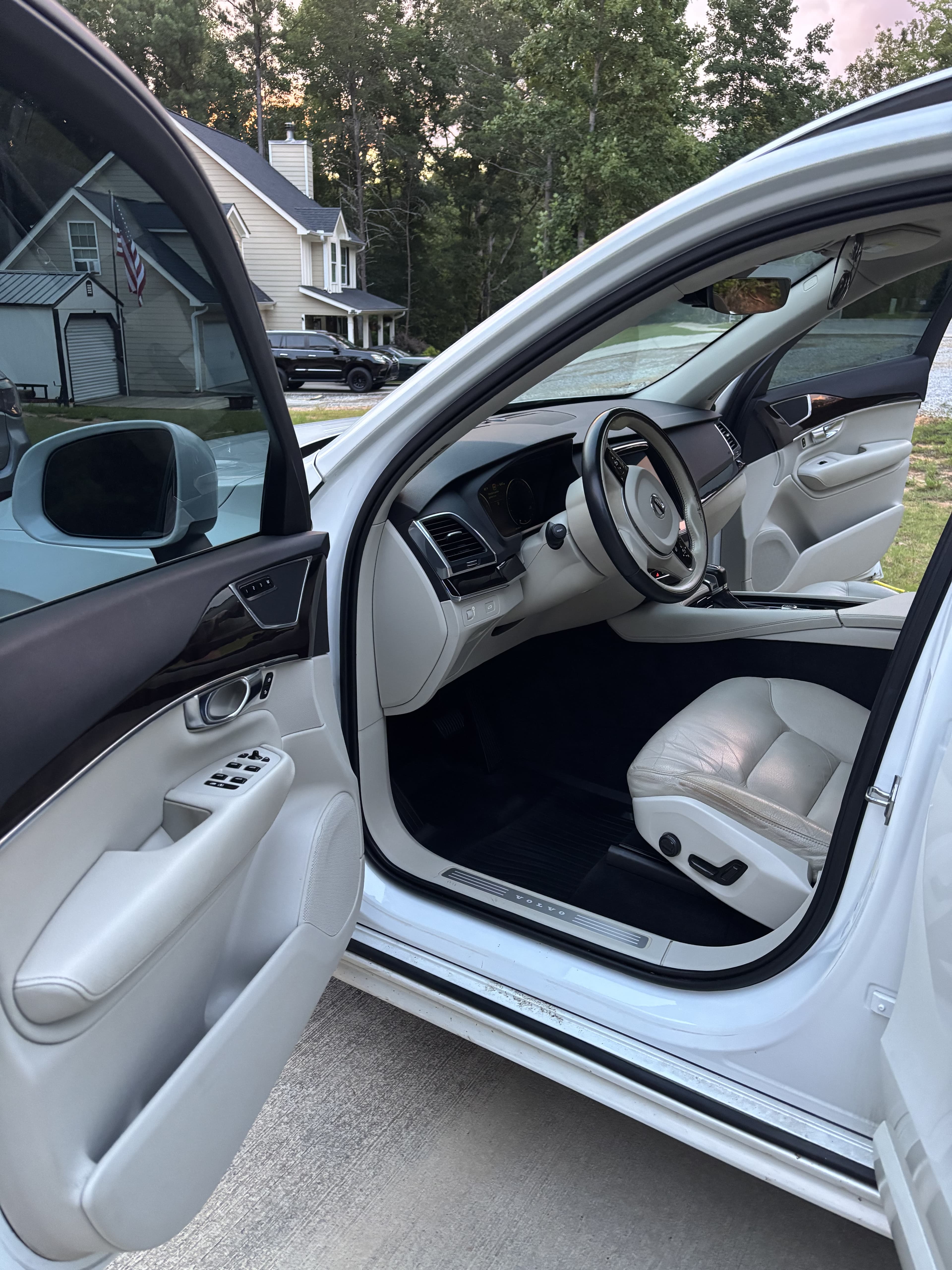 Open driver's door of a white Volvo showing light leather interior and modern dashboard.