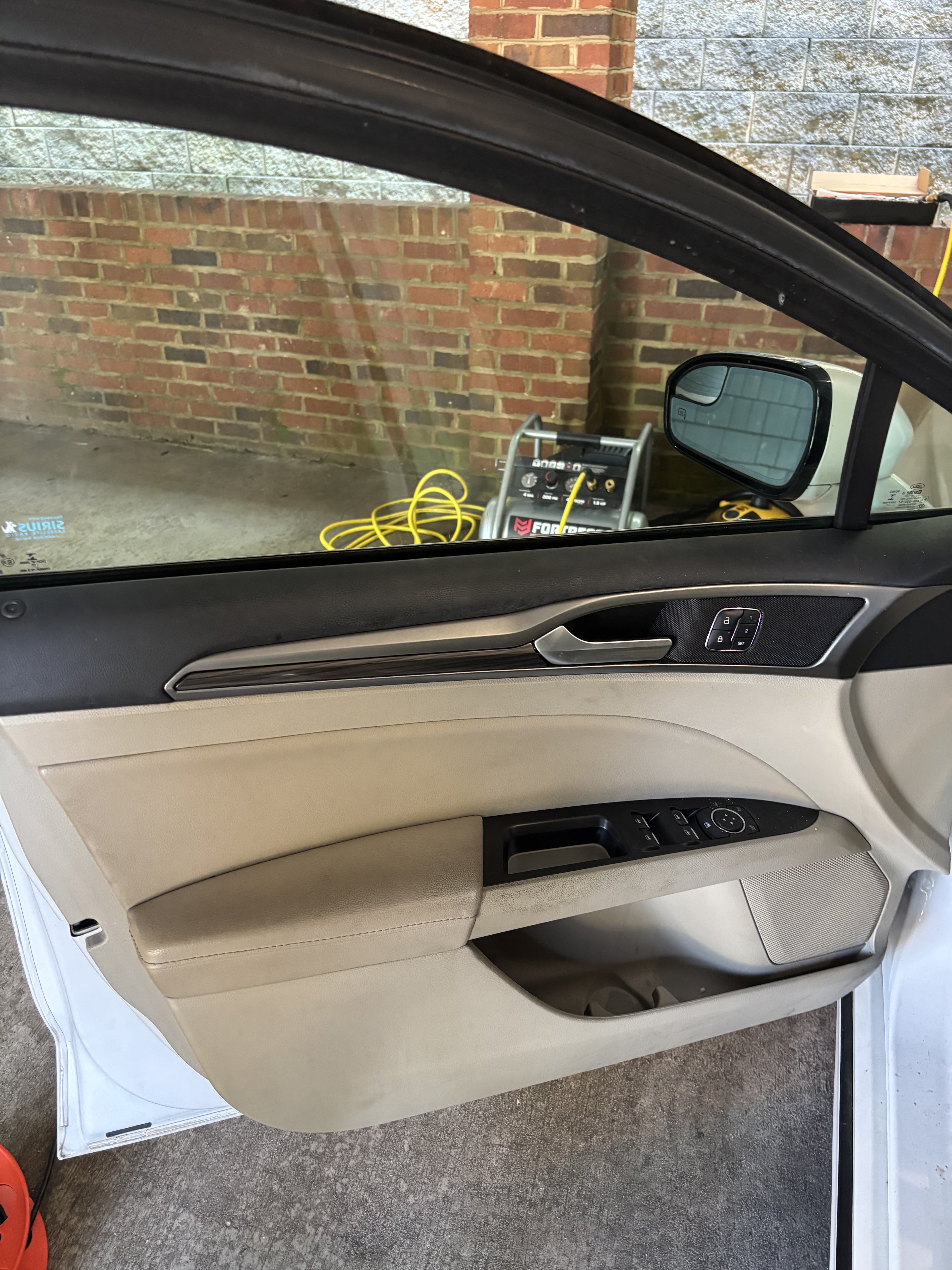 Beige car door interior with black trim, silver handle, power window controls, and side mirror.