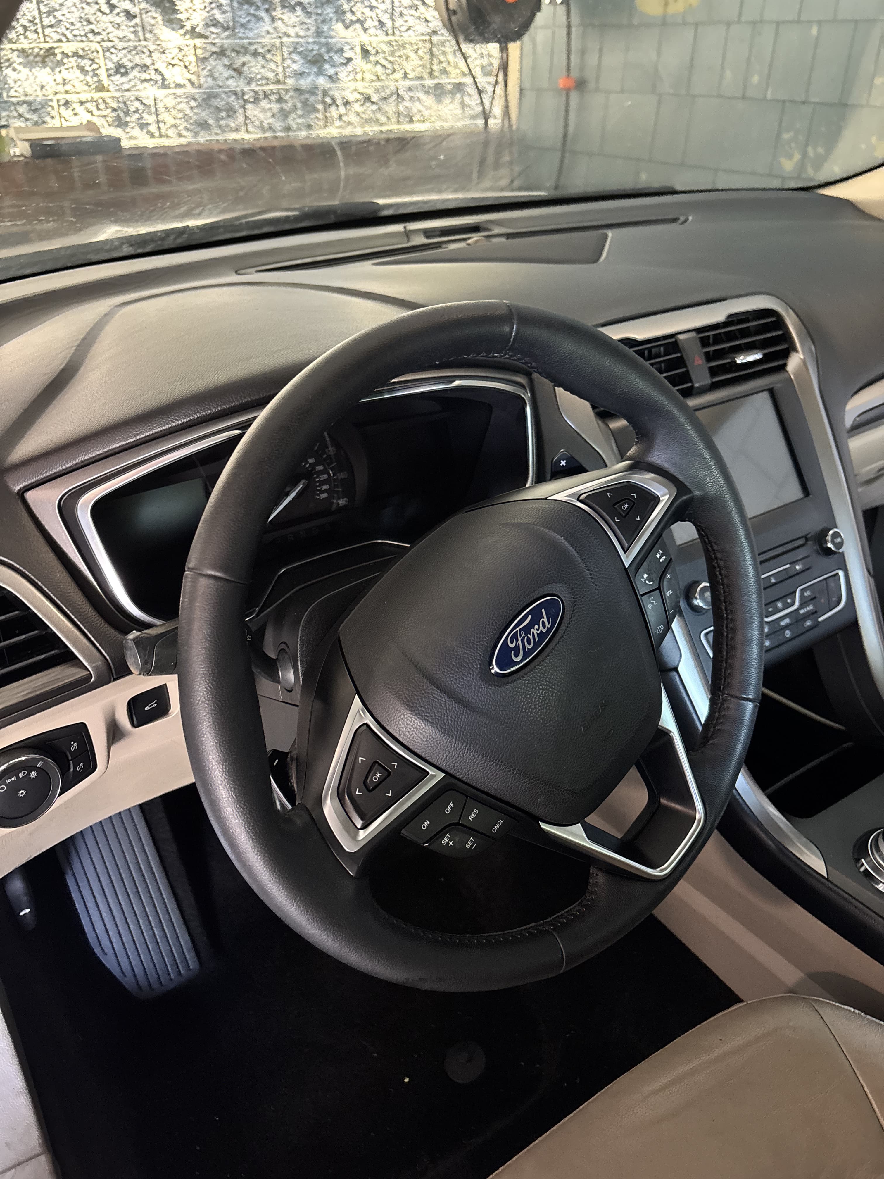 Black leather-wrapped steering wheel with Ford logo inside a car with a modern dashboard.